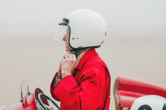 a man in a red jacket and white helmet standing next to a red race car