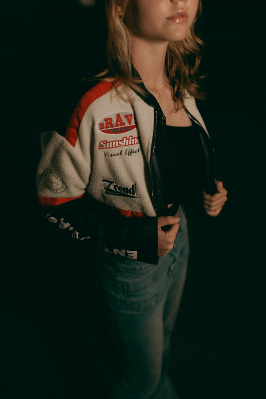 A woman poses, wearing a bomber jacket.